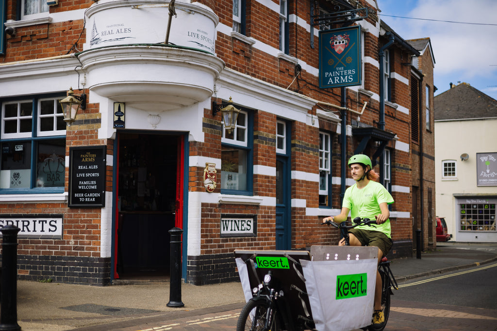 Person on a bicycle with a 'keert' bag in front of a brick building with signage.